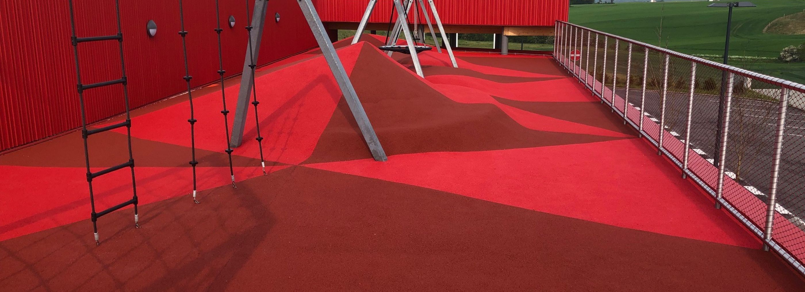 Outdoor playground with climbing frames with the entire floor made with red coloured rubber granules.