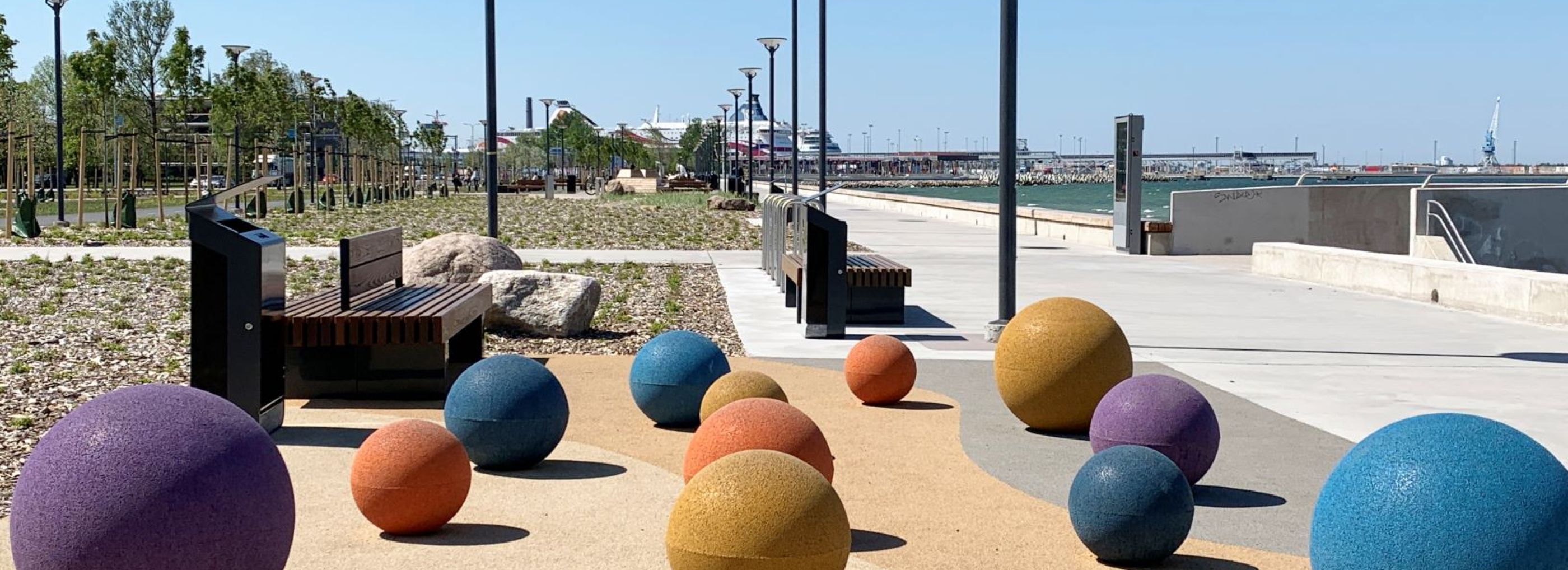 Collection of various sized rubber spheres in different colours set along a coast line.