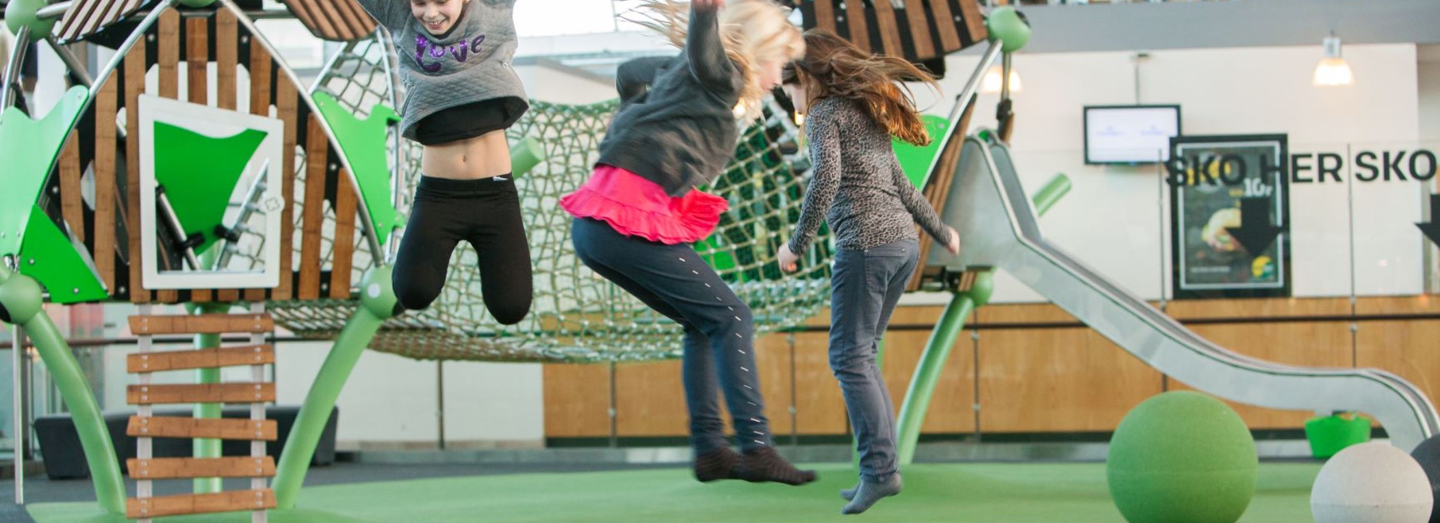 Three girls jumping on an indoor rubber floor playground.