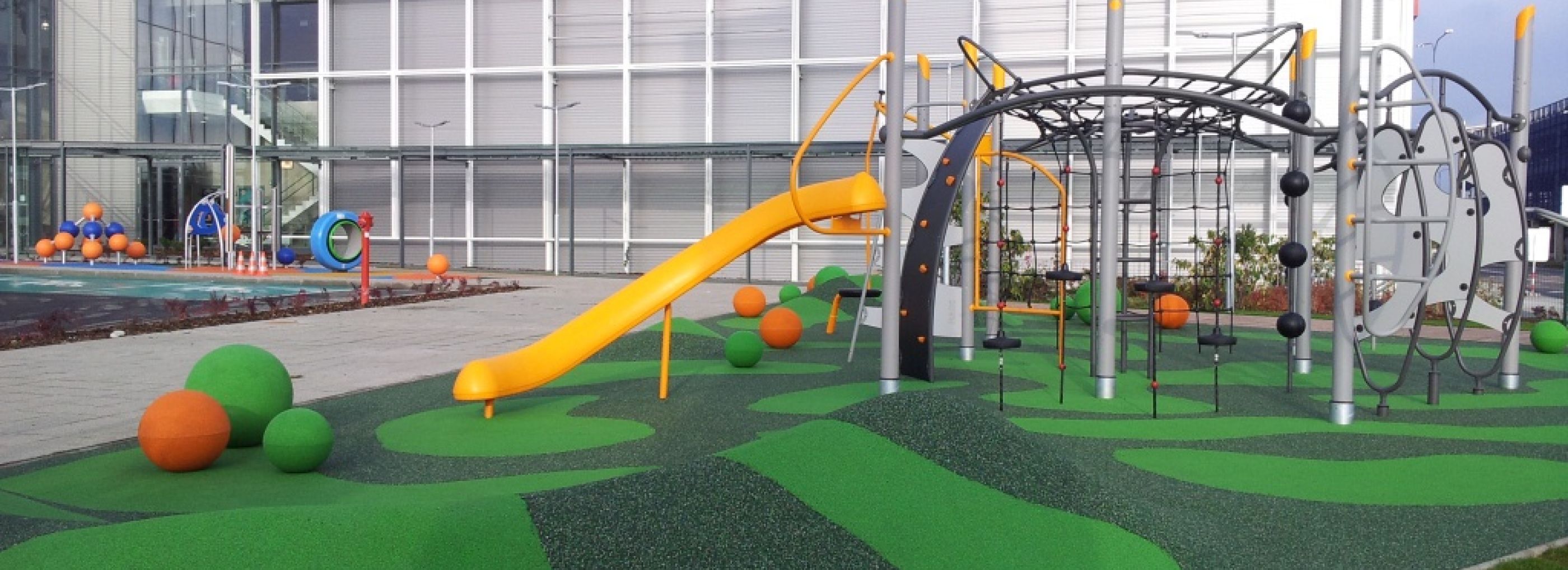Outdoor climbing frame with green rubber flooring and green & orange spheres.